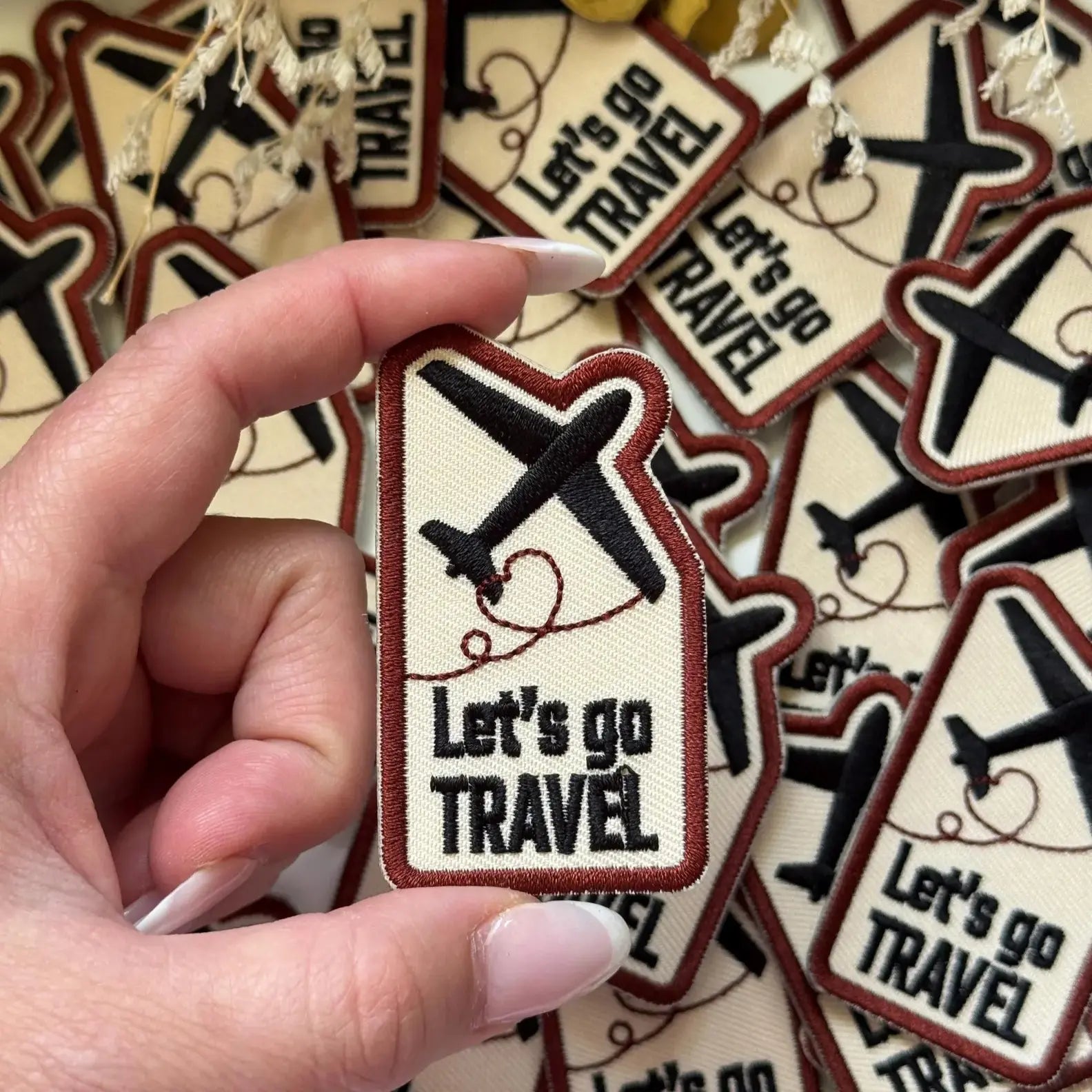 Hand holding a 'Let's go Travel' patch with more patches in the background.