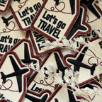 Collection of 'Let's go TRAVEL' patches with airplane icons on a textured surface.