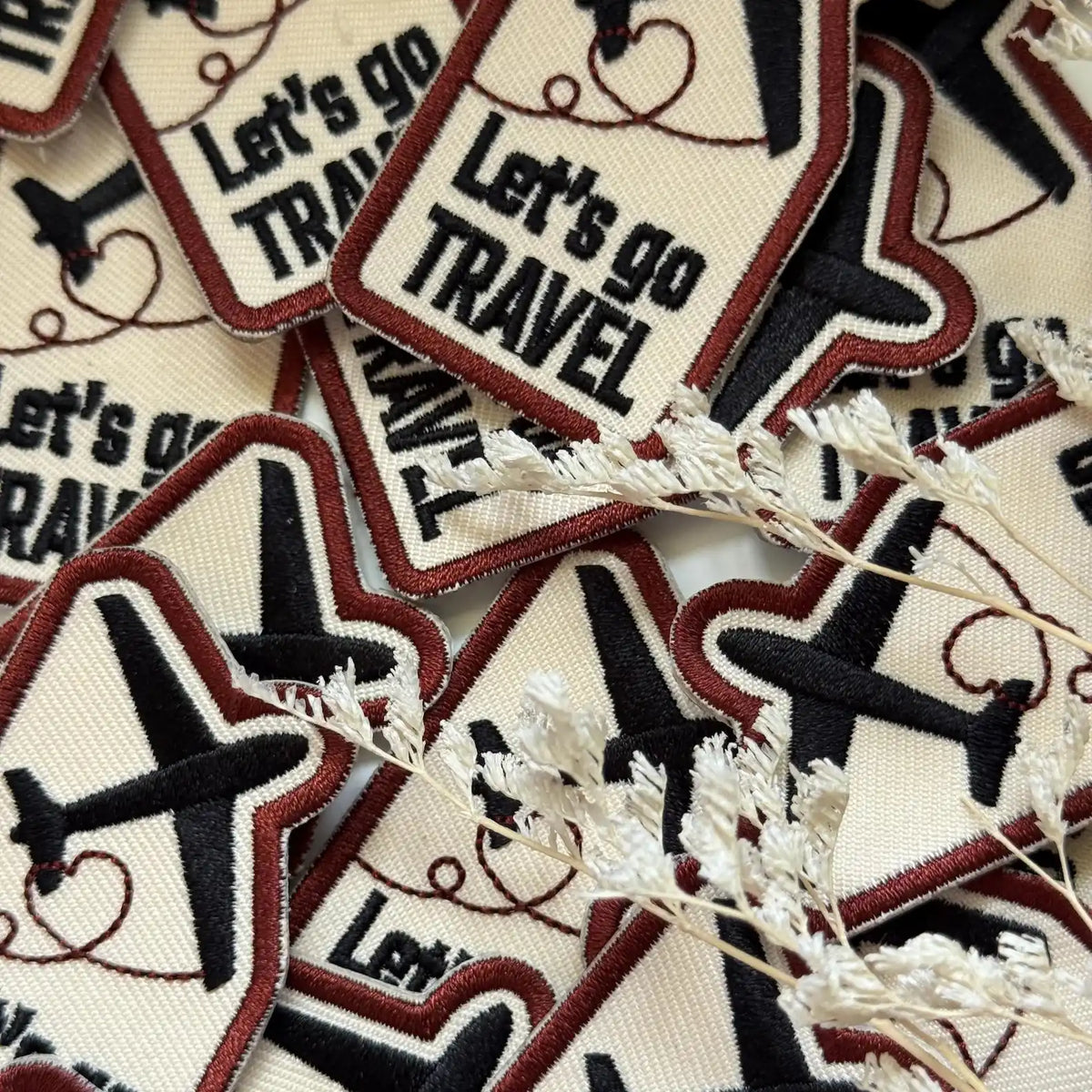 Collection of Let's Go Travel Embroidered Patches with airplane icons on a textured surface