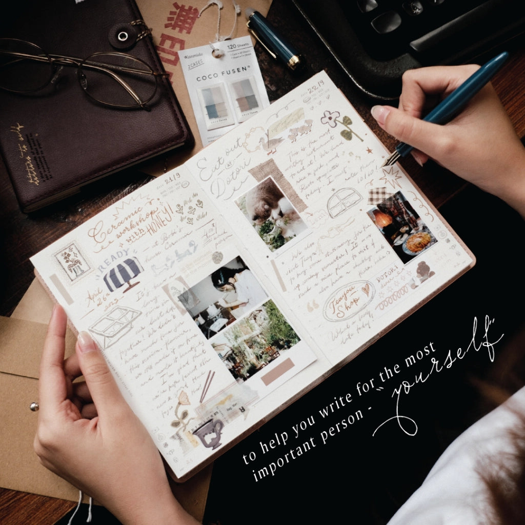 Person holding a journal with photos and text on a desk with stationery items.
