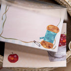 Notebook with a yarn ball illustration on a decorative tray with apples and chocolate.