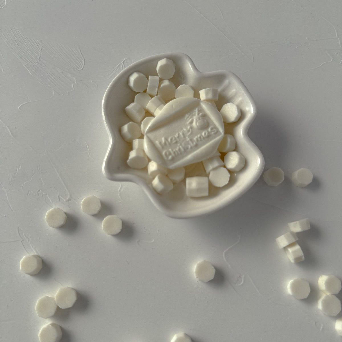 Light Ivory Wax Beads with a Happy Christmas stamped seal on a grey surface, creamy beads scattered around
