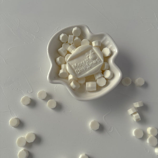 Light Ivory Wax Beads with a Happy Christmas stamped seal on a grey surface, creamy beads scattered around