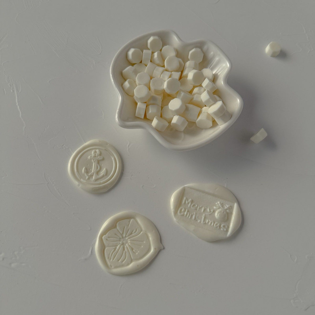 Light Ivory wax beads in a mold with three decorative stamped seals on a grey surface, overhead view