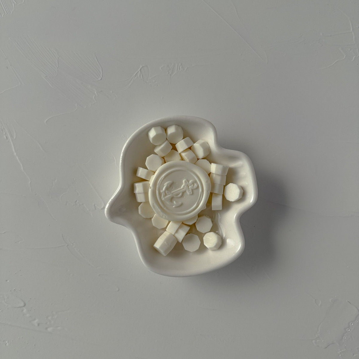 Stamped Light Ivory wax seal with an ornate design displayed on a ceramic base, close-up on grey