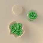 Green candy pieces in a jar and on a plate on a light beige background