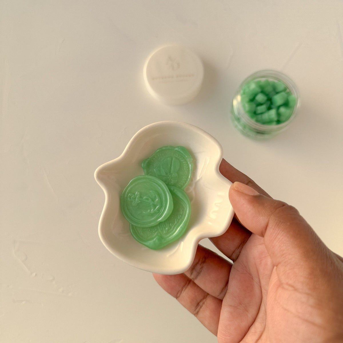 Hand holding a small white dish of vivid lime green Lime Life sealing wax beads, close-up detail shot