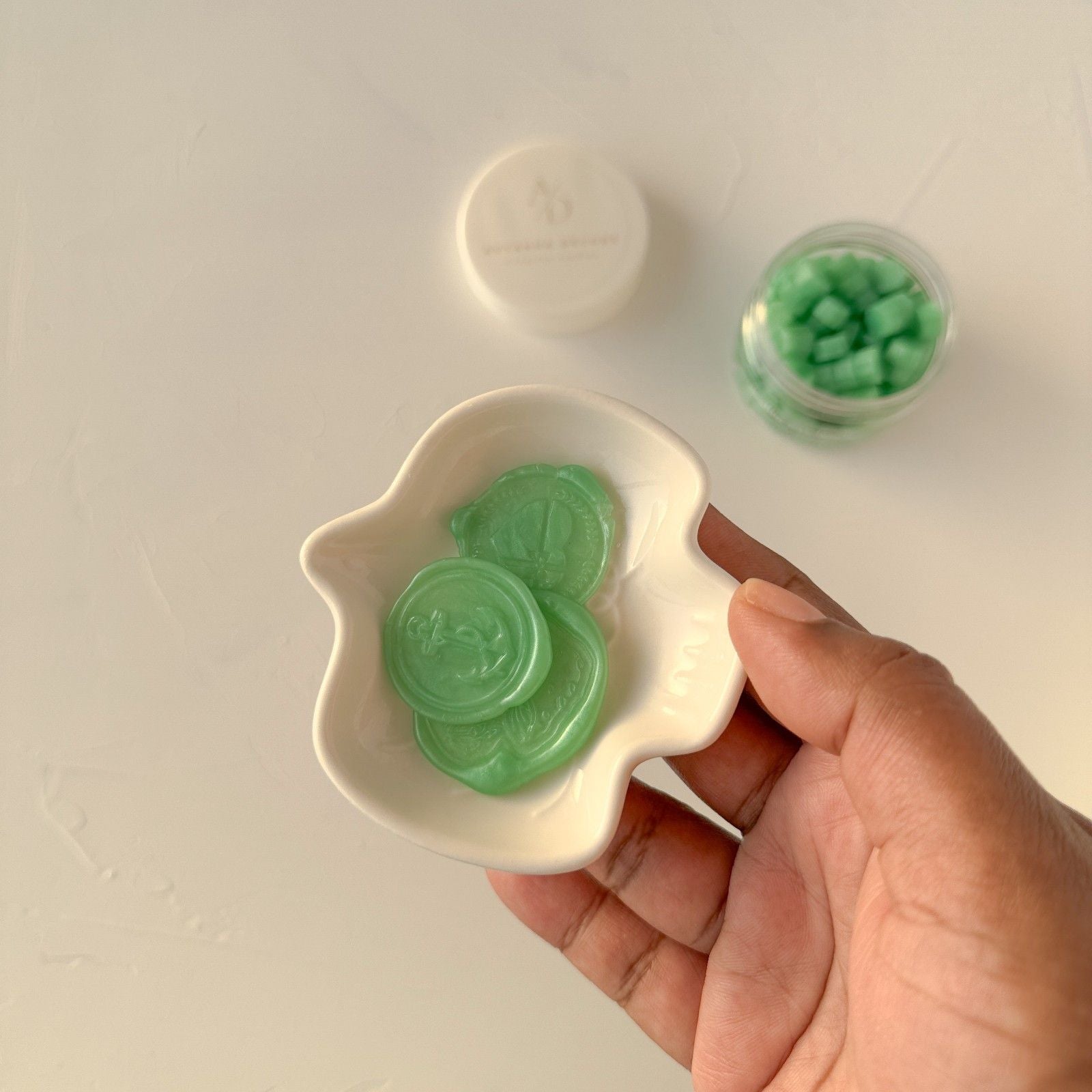 Hand holding a small white dish with green jelly-like candies on a light background