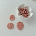 Pink wax seals on a white surface with a small white dish containing more pink wax seals.