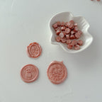 Pink wax seals on a white surface with a small white dish containing more pink wax seals.