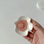 Hand holding a small white dish with pink circular objects on a light gray background