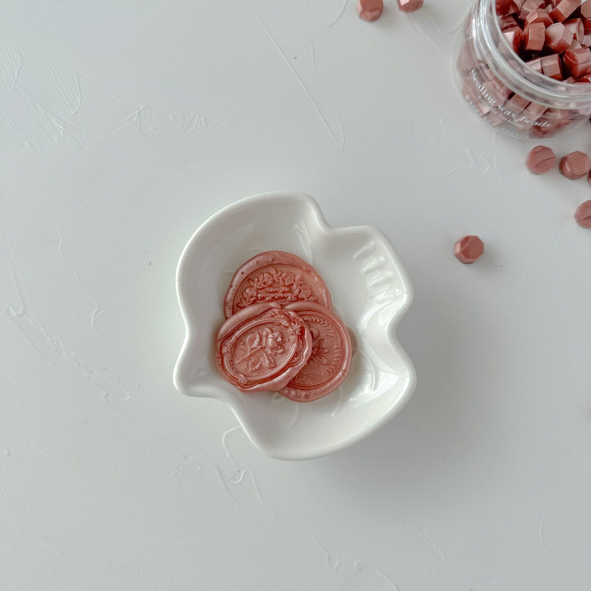 Round Lingering Brew sealing wax beads gathered in a small white dish, close-up on a soft grey studio backdrop
