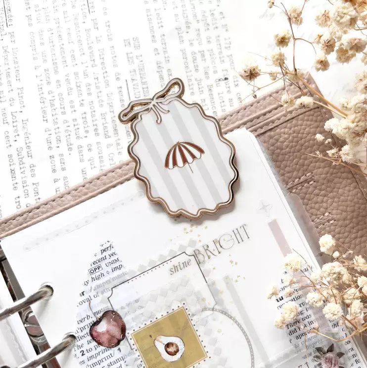 Little Delights Enamel Journal Clip with shell design styled on a book with flowers