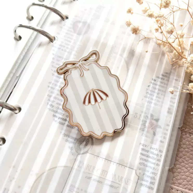 Shell-shaped Little Delights Enamel Journal Clip on a notebook page with dried flowers