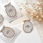 Decorative pendant with striped design on a white card, surrounded by dried flowers.