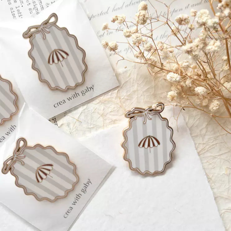 Striped Little Delights Enamel Journal Clip on a white card surrounded by dried flowers
