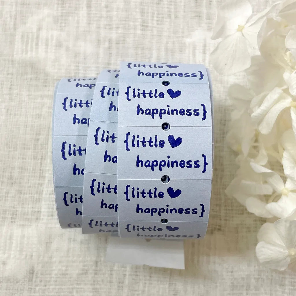 Roll of decorative tape with 'little happiness' text on a textured surface.