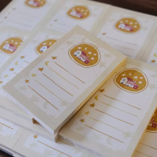 Stack of Little Village Memo Pads with decorative village covers on a wooden surface