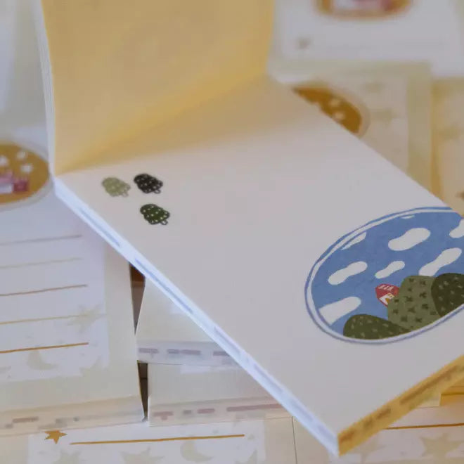 Little Village Memo Pad sheets with colorful designs displayed on a wooden surface
