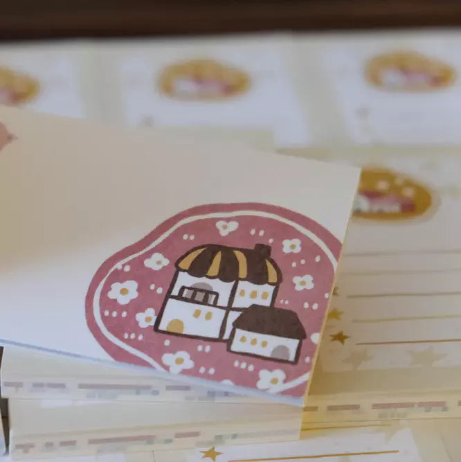 Stack of Little Village Memo Pad cards with a cute house design on a pink background