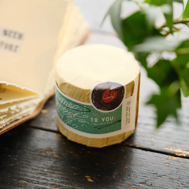 Small paper-wrapped bottle with a green Love Label Rubber Stamp tag on a wooden surface
