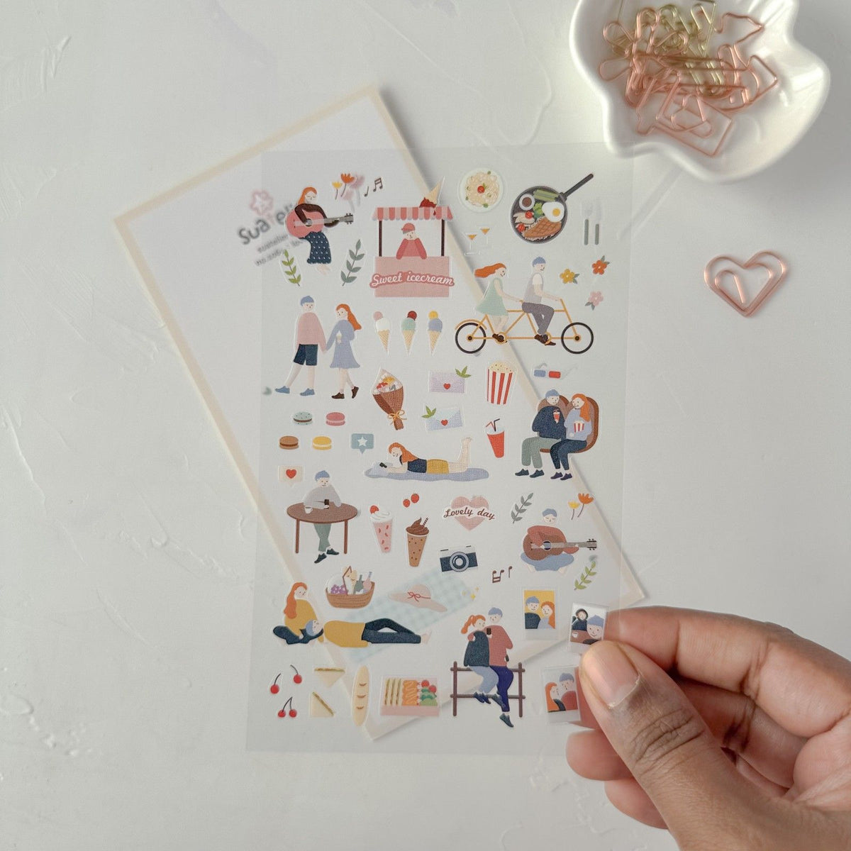 Sheet of illustrated stickers held by a hand on a light surface, from the Lovely Day Sticker Sheet