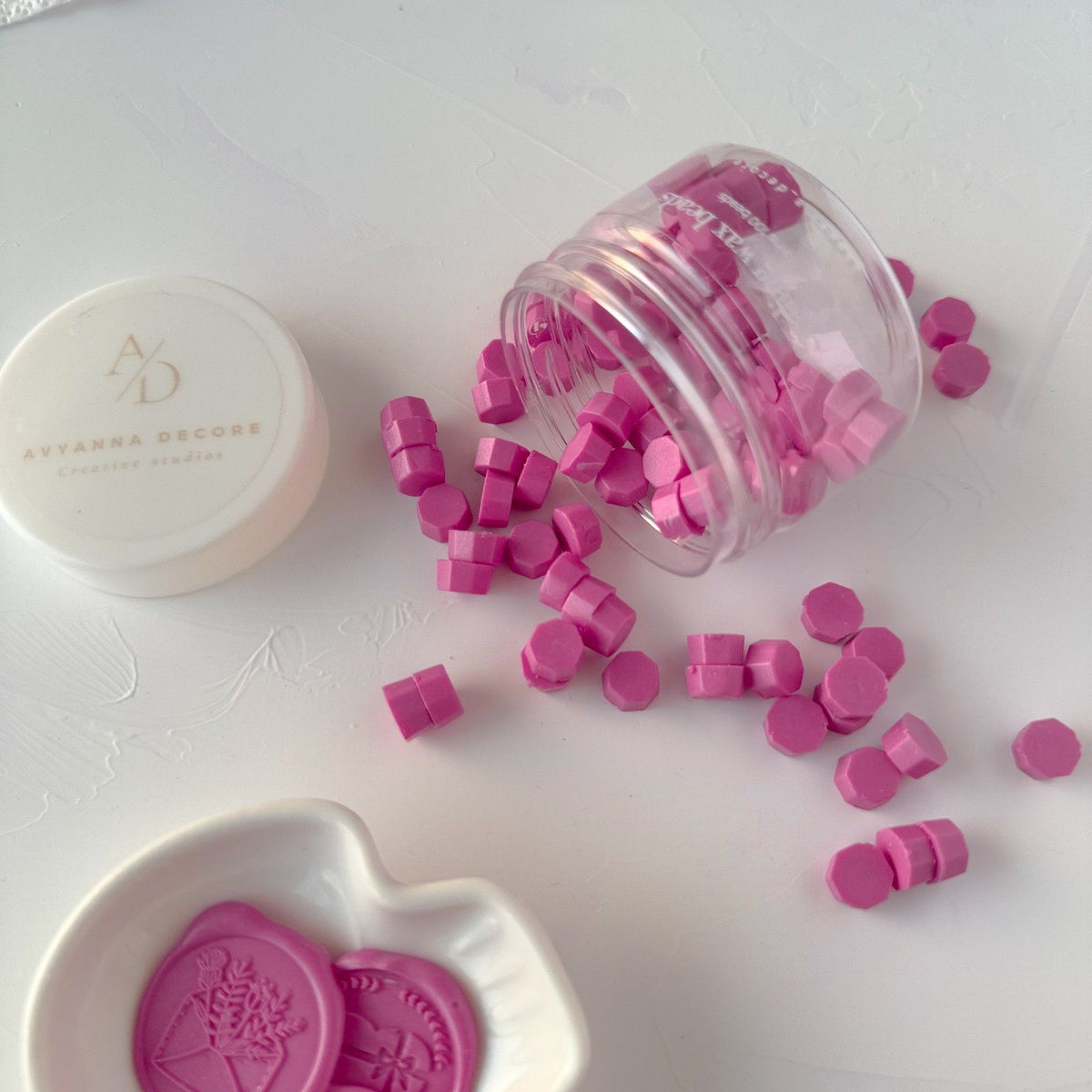 Hexagonal Magenta Pink wax beads spilling from a clear container onto a white surface, close-up detail