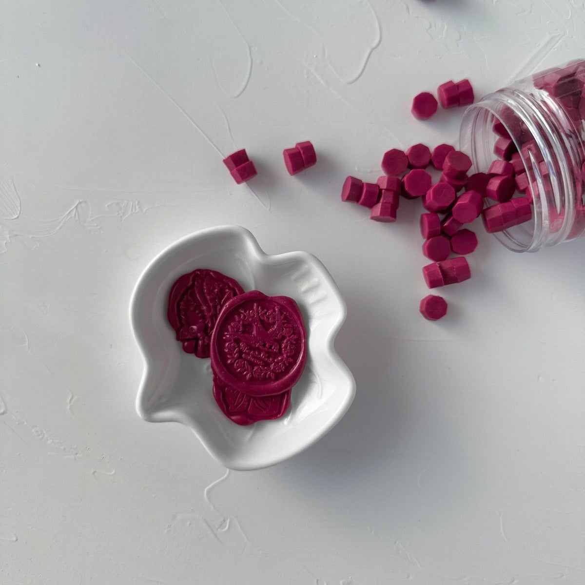 Magenta Rush Wax Beads and broken bead pieces showing their rich pigment, flat lay on a white surface