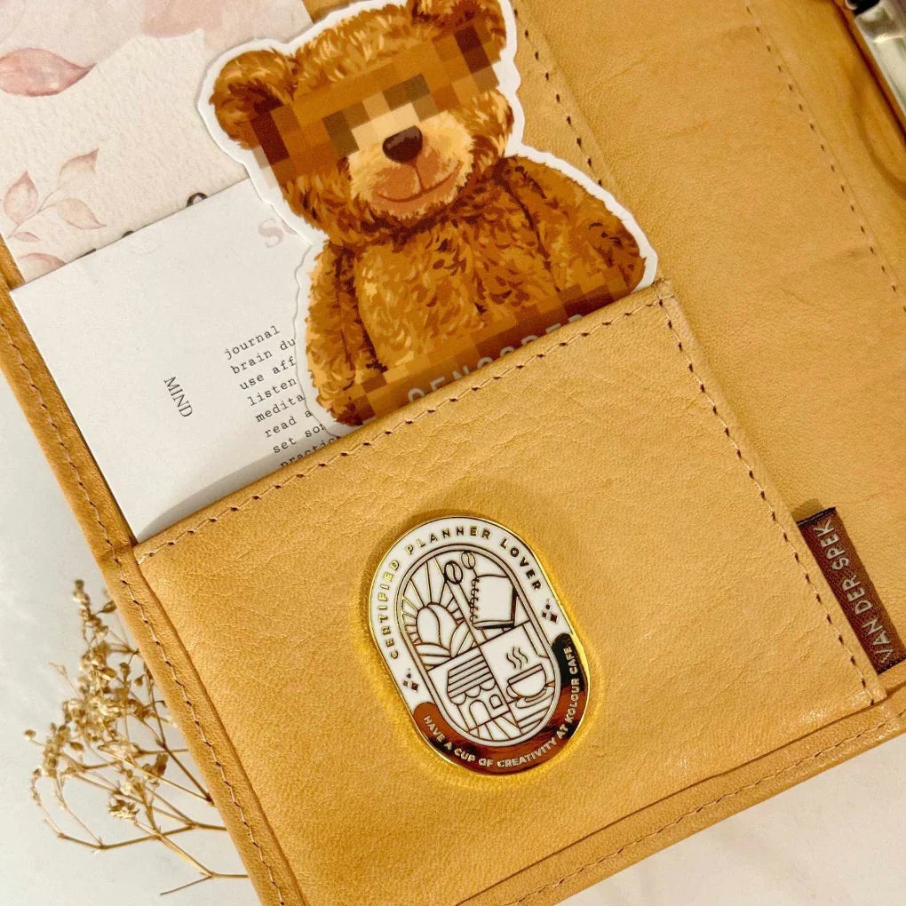 Planner Lover Badge Magnetic Charm attached to a tan leather planner pocket, cafe-themed enamel