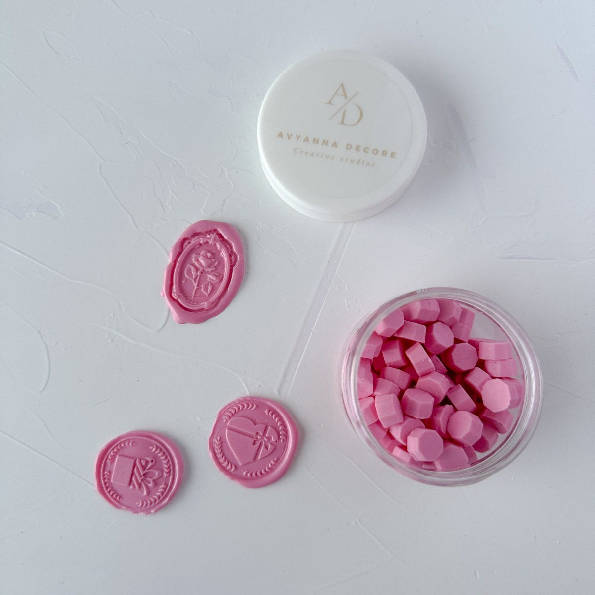 Delicate Maiden Pink sealing wax seals beside the open container of pink beads on a clean white backdrop