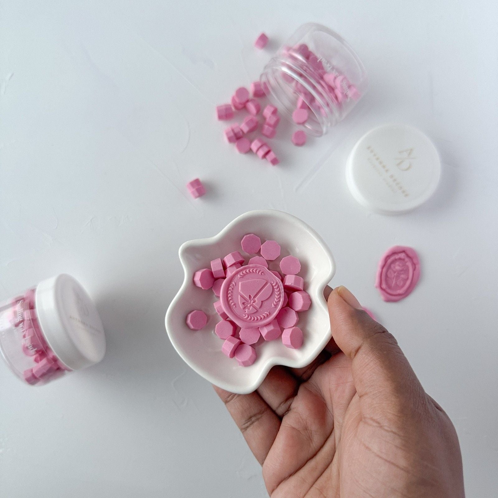 Pink decorative stamps in a white container held by a hand on a light gray background