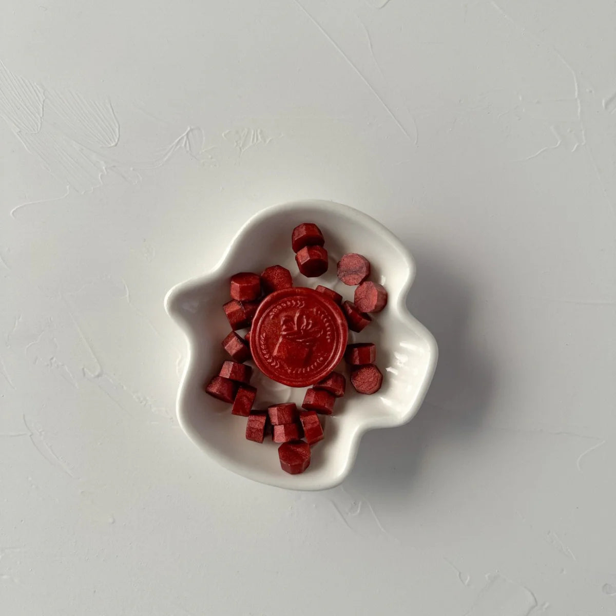 Maroon Wax Beads in a deep red cube shape filling a white dish with a stamped wax seal at the centre