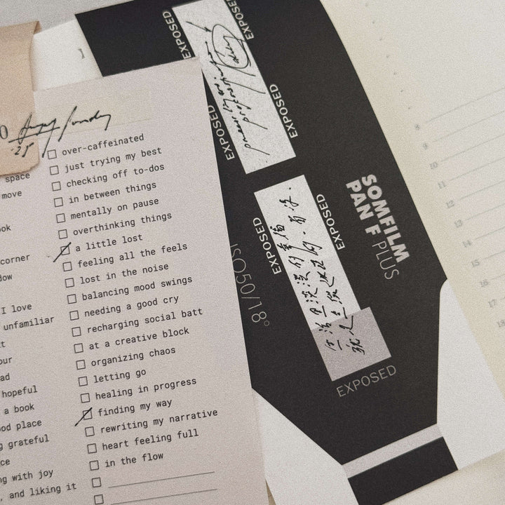Film canister labeled 'SOMEOFILM PAN F PLUS' with a checklist on a textured surface