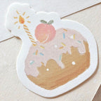 Pastel aesthetic birthday cake memo pad shaped like a donut with icing, sprinkles, peach topping, and a lit candle illustration
