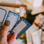 Hand holding two blue and white cards with decorative borders.