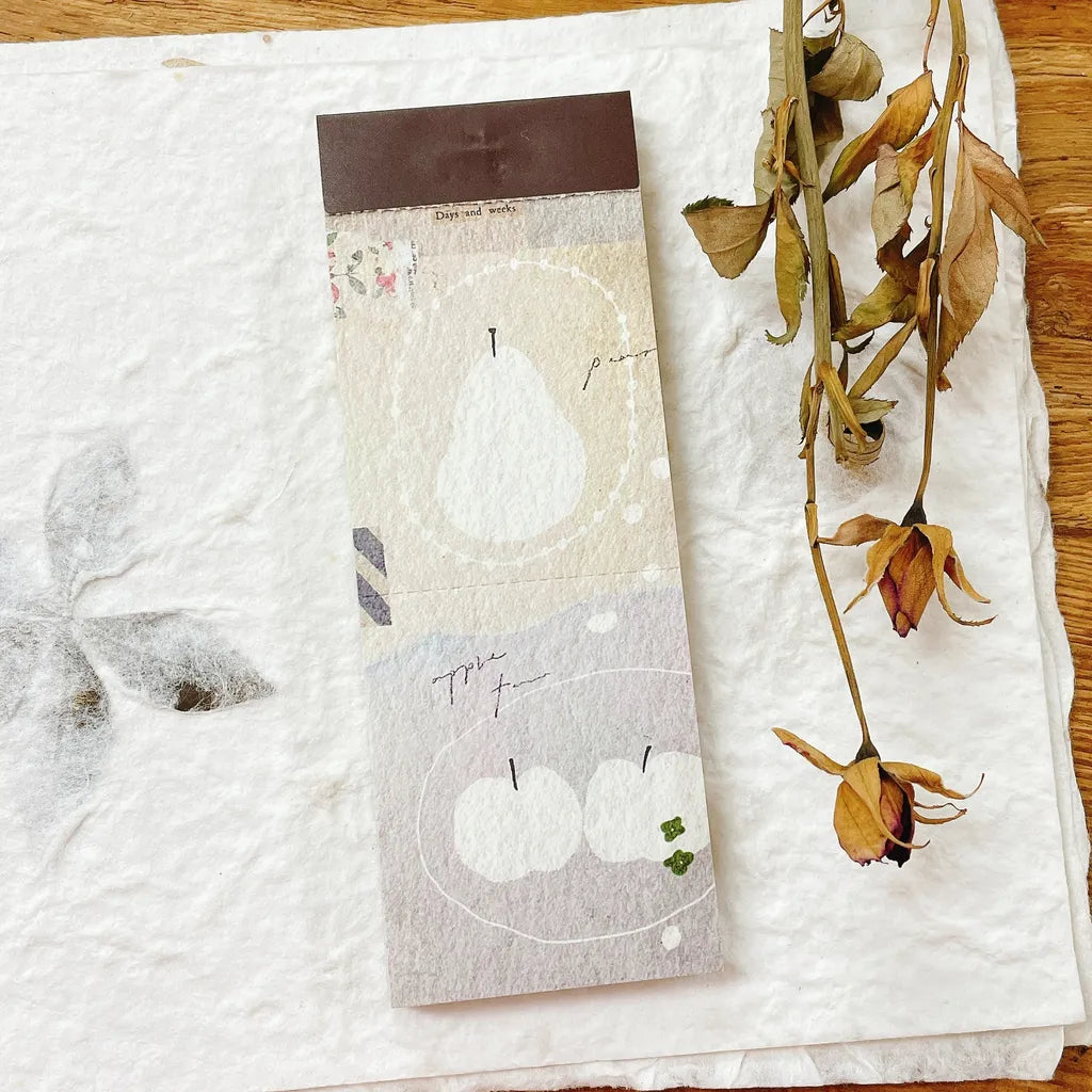 Appear Memo Pad Vol. 3 apple design styled as a roll with dried flowers on a white surface