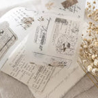 Sheet of decorative stamps with vintage design elements on a textured surface with dried flowers.