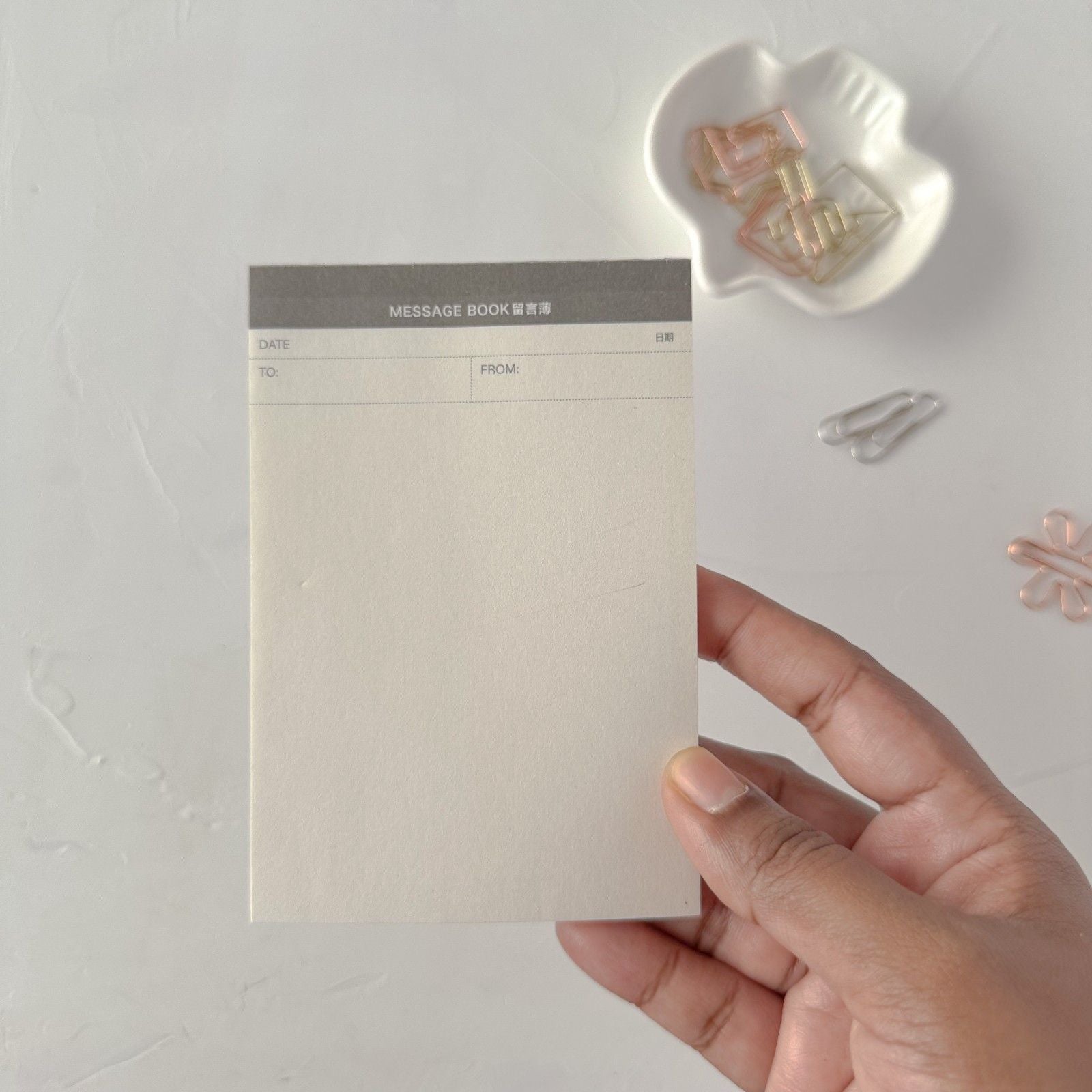 Hand holding a small white card with decorative elements on a light gray background