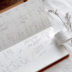 Open notebook with handwritten notes on a white surface with dried flowers.