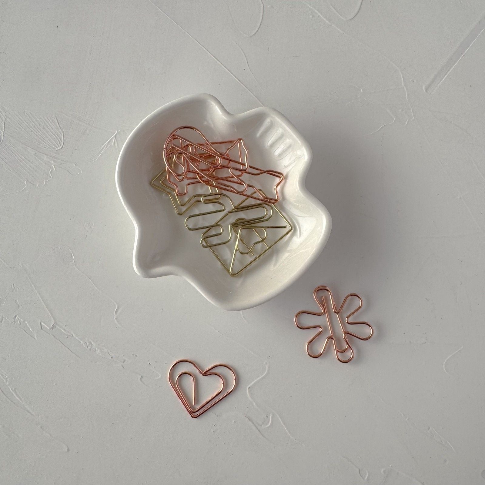 Rose gold paper clips on a white dish and surface