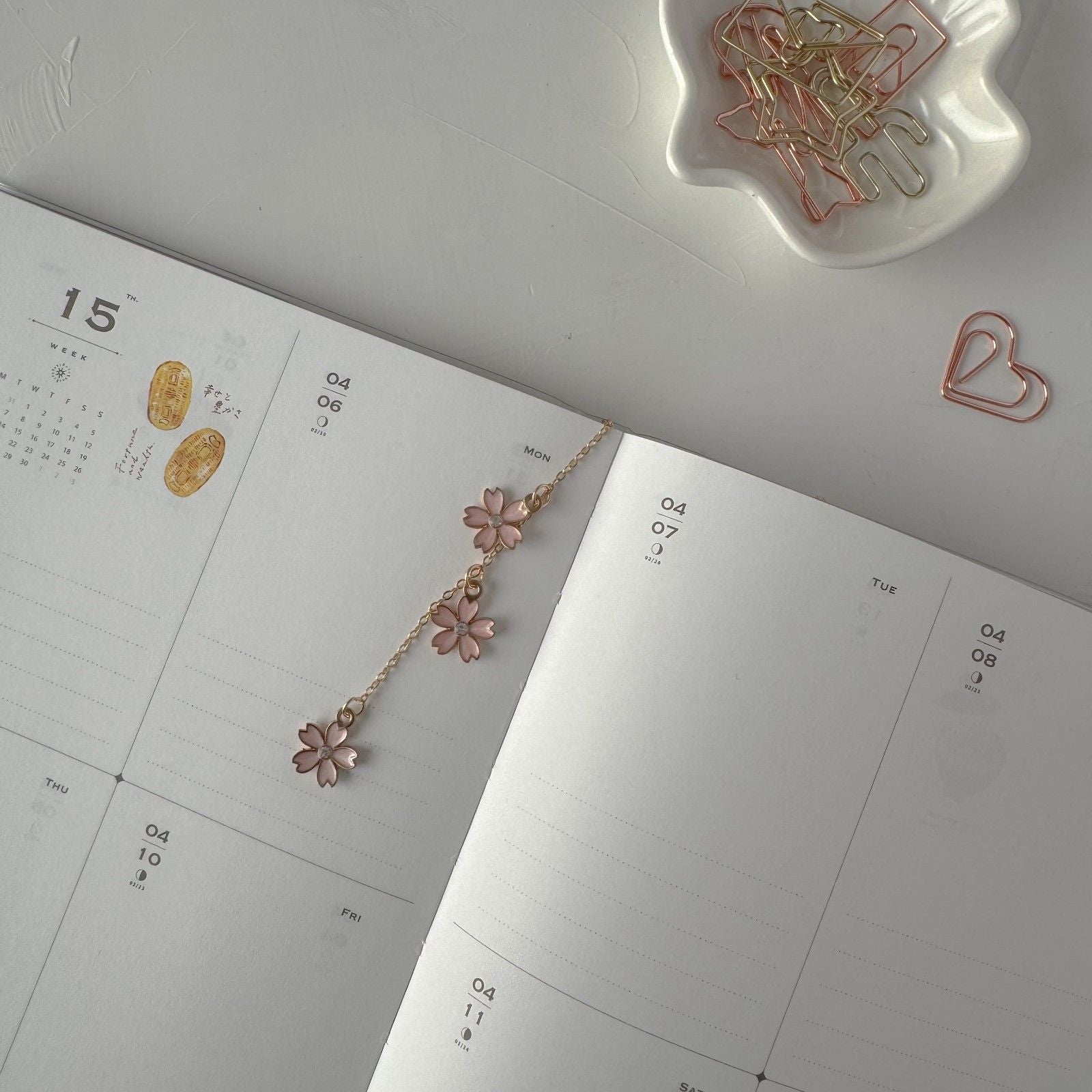 Floral necklace on an open planner with decorative paper clips on a light gray surface.