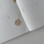 Gold necklace with a decorative pendant on an open planner.