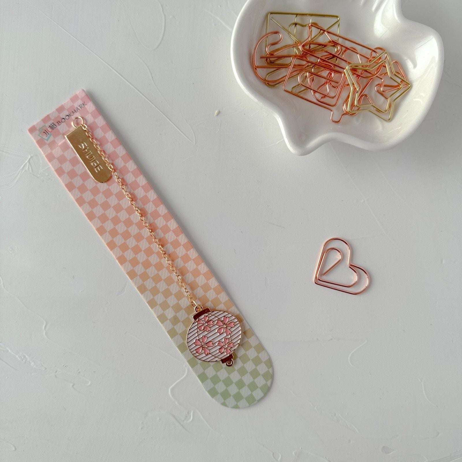 Decorative bookmark with gold chain and heart-shaped paper clip on a white surface