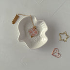 Necklace with a heart pendant on a white dish, surrounded by decorative items on a light gray background
