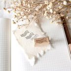 Wooden stamp with wavy design on a piece of paper with dried flowers and a pen.
