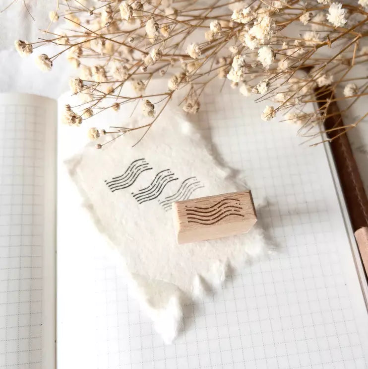 Mini Postal II Rubber Stamp with wavy postmark design on paper with dried flowers and a pen