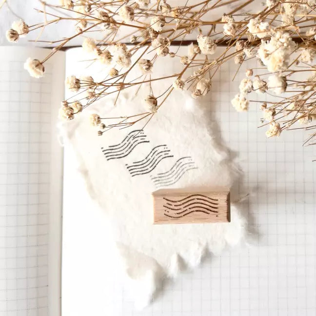 Mini Postal II Rubber Stamp wavy line design on a white surface with dried flowers around