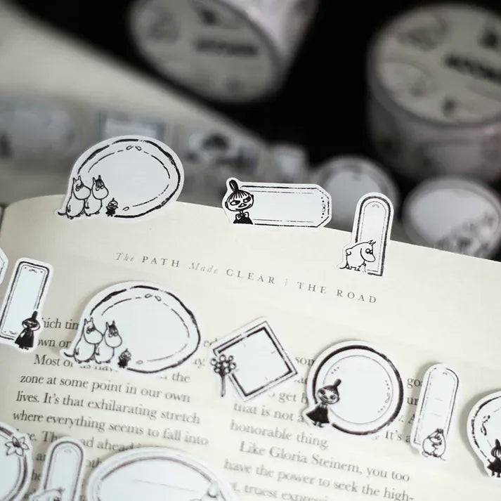 Black and white Moomin Label Sticker Tape illustrations on a book with washi rolls in the background