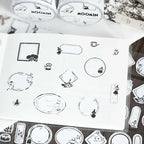 Sheet of black and white stickers with Moomin characters on a wooden surface.
