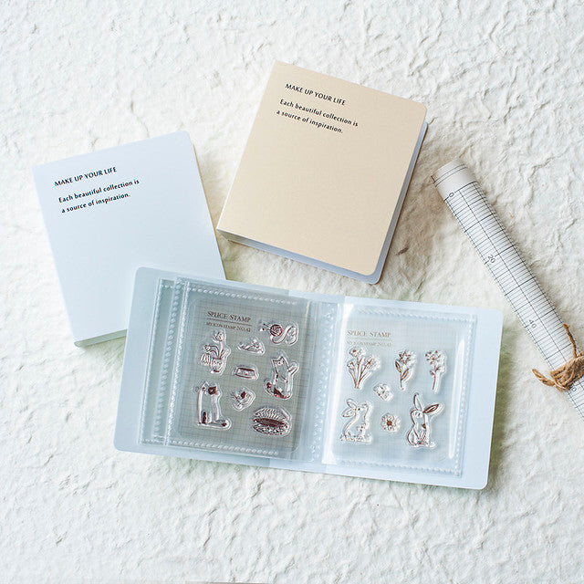 Set of clear stamps in an open book on a textured white surface with notebooks and a ruler.